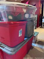 Five plastic storage tubs stacked containing assorted Christmas decorations including soft decor and nativity scene items as seen from the outside