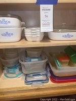 Shelves with stacked vintage CorningWare bakeware featuring blue floral design and multiple plastic food storage containers with assorted lids.