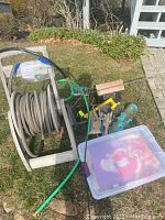 Wide view showing garden hose on winding reel cart, garden tools, bird feeders, and plastic container with seasonal garden banners