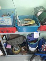 Photo showing plastic bins filled with gardening gloves, tools, partially used plant food, and a collection of ceramic pots on a lower shelf.
