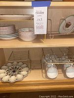 Shelf displaying stack of teacups, saucers, sugar bowl, small bowls, storage racks with deviled egg plate and cups stored