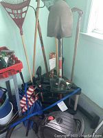 Gardening tools grouped in corner: shovels, hedge trimmer on caddy, shop vac at base