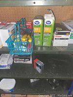 Shelf with assorted light bulbs including GE soft white and Philips halogen, boxes of dishwasher pods, and small hand tools in blue basket.
