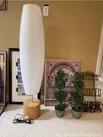 Full view of modern lamp with white paper balloon shade on wooden base, two faux ivy topiaries, trompe l'oeil panel, and metal decorative hanging display with faux fruit