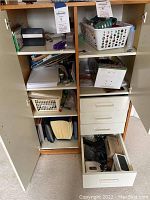 Front view of the wooden office cabinet with both doors open showing shelves and drawers filled with office supplies including baskets and files.
