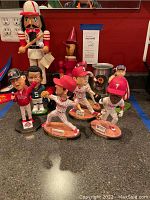 Front view showing multiple Phillies baseball player bobbleheads on countertop with a nutcracker bobblehead in the background and some misc items