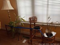 Full view of lot with rattan plant stand, two metal plant stands, bamboo end table, and brass and marble lamp with shade.