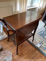 Dark wood tea cart viewed from the side with drop leaf sides folded down, showing the wheels and lower shelf.
