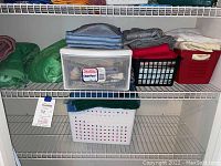 Wire shelving with folded towels in green, terracotta, gray, blue, red, and cream along with bins possibly containing linens and window treatments.