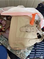 Beige handbag with buckle on table among other items.