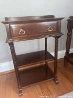 Front view of the larger dark mahogany vintage side table showing the drawer with brass handles, turned legs, and two lower shelves.