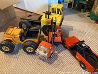 Five Tonka trucks displayed on carpeted floor in various colors and sizes
