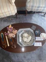 Overview of all items set on wooden oval table between two upholstered chairs, showing arrangement of candle sconces, bowls, ceramic fruit, Lenox vase with dried flowers, stained glass coaster set, and Royal Imperial teacup with saucer.