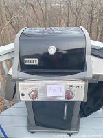 Front view of Weber Spirit propane gas grill showing black lid with thermometer and stainless steel front control panel with two red marked knobs.