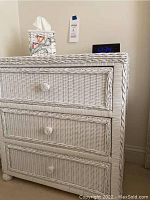 Front view of white wicker 3-drawer chest with tissue box and digital clock on top showing 12:34.