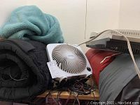 White Living Solutions table fan with dial control placed on top of rolled black blankets and air mattresses