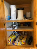 Kitchen cabinet shelf with two air popcorn poppers, cords visible, and food storage boxes on lower shelf including plastic wrap and aluminum foil.