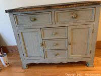 Front view of the wooden cabinet showing five drawers in the center and one cabinet door on each side. Wooden knobs on all drawers and doors.
