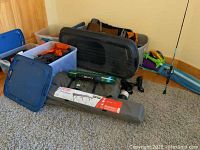 Four plastic totes filled with various camping equipment; fishing pole leaning on the wall; tent and cot bags on the floor