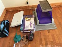 Photo of cat litter box, cat carrier, box of litter trays, blue mouse toy, green pet accessory on hardwood floor