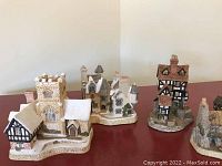 Five David Winter miniature Christmas houses arranged on a red surface; scene shows multiple houses with snow-covered roofs depicting a winter village.
