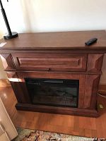 Front view of wooden cabinet fireplace unit with drawer front and remote control on top.