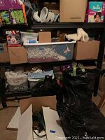 Metal shelving rack holding multiple plastic tubs, cardboard boxes, holiday decorations including a plush white figure and Star Wars item.