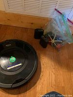 Full view of iRobot Roomba vacuum, accessories in plastic bags, and electronic fence units on wooden floor.
