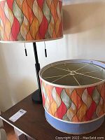 Photo showing two cylindrical lamp shades with colorful abstract wavy pattern in red, orange, yellow, green and beige.