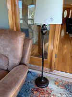 Full view of one floor lamp showing brown leather couch, wood floors and glass door behind.