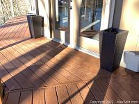 Photo showing two tall, black faux wicker planters placed on wooden deck flanking glass door.