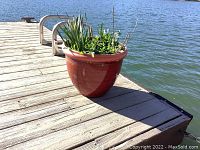 Red plastic planter with green plants and solar outdoor light on a dock near water