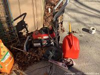 Pressure washer unit with hose and spray wand lying on driveway beside gas can and gardening supplies
