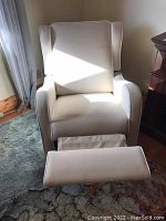 Front view of a beige canvas recliner chair with white piping and extended footrest, showing shape and upholstery condition.