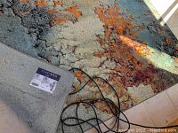 Top view of the area rug showing abstract blue, copper, red, and black colors and pattern with an electrical cord on top