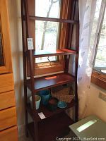 Full view of the wooden ladder shelf with five shelves angled against a window with curtain showing the design and wood finish.