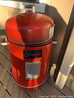 Front view of the red Brinkmann Gourmet electric smoker showing the wooden handle on the lid, front access door, and the brand emblem.