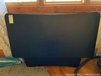 Front view of the black rectangular desk top with a slightly curved front edge, resting vertically against a wall.