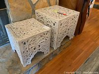 Two carved solid wood decorative tables positioned side by side on a hearth shelf, showing full top and side carved ornamentation.