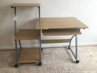 Full view of the computer desk showing main desktop, side shelves, keyboard tray and wheels.