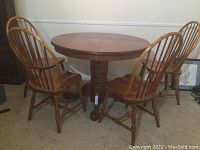 Full view of round wooden dining table with four matching wooden chairs with spindled backs.