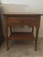 Front view of wooden nightstand showing drawer with metal handle and lower shelf, slight scratches and wear visible.