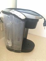 Side view showing clear water reservoir attached to black machine base with power cord and drip tray.