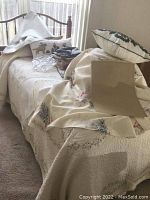 Bed with cream-colored quilted bedding, various linens, and decorative throw pillows placed on it. Items appear gently used and holiday themed.