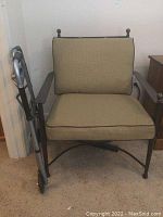 Metal patio chair with beige cushions, black piping and folding metal walker placed next to it.