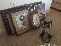 Photo showing two black metal battery-powered wall sconces with frosted glass shades, six framed wall art prints, and a Seiko octagonal wooden-framed clock with Roman numerals.