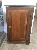 Front view of wooden trash bin cabinet with door closed, showing natural wood finish and knob handle.