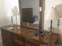 Photo of dresser top showing entire lot items: two brass lamps with cream lampshades, Waterford crystal clock, digital alarm clock, metal key and calculator with mirror in background.