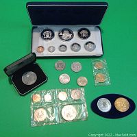 All coins laid out on green background: proof set case open showing 8 coins, black box coin, oval display, sealed plastic bags and loose coins
