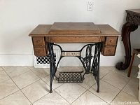 Front view of closed wooden sewing table with SINGER treadle base and four drawers.